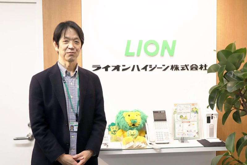 企業ロゴの前に立つ内垣さん